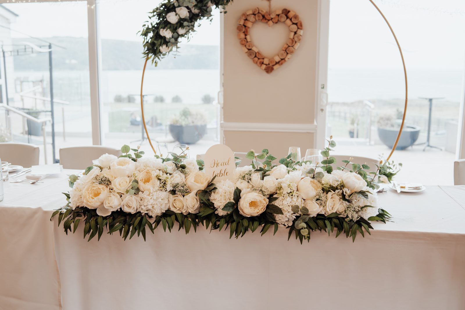 Gold hoop arch with ivory florals behind a top-table flower arrangement
